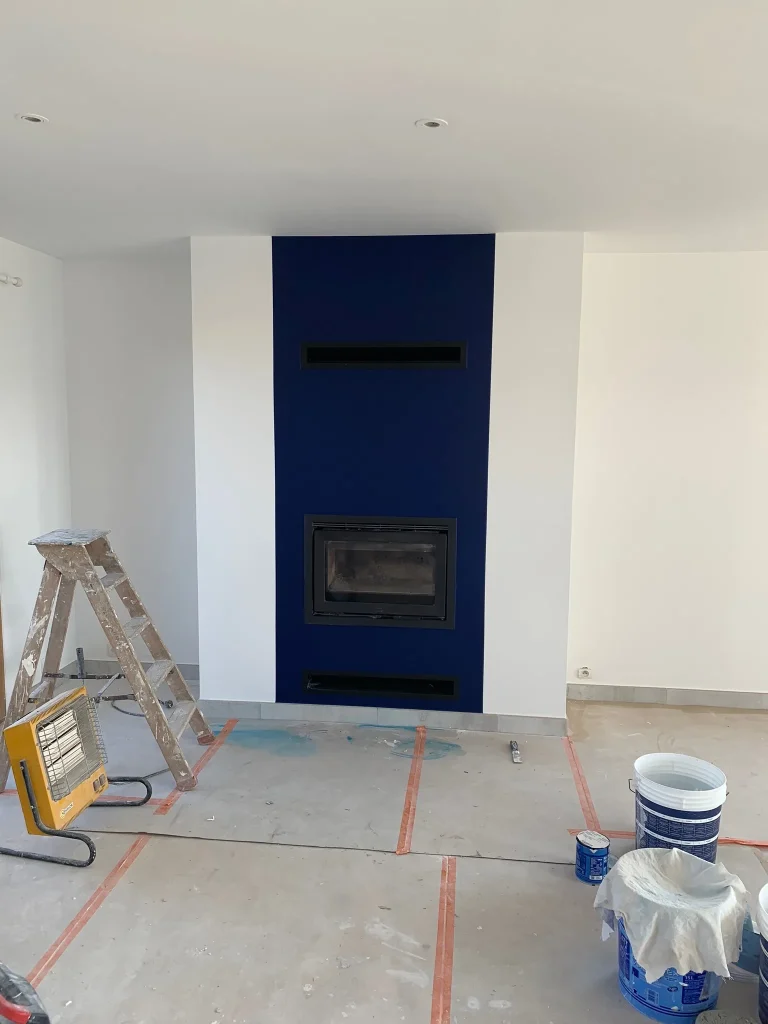 Pièce en rénovation avec murs blancs et bande verticale bleue autour d'une cheminée
