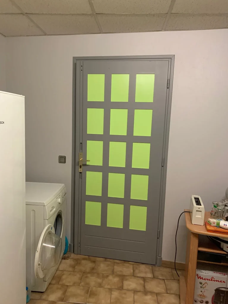 Porte intérieure grise à panneaux verts, entre deux murs blancs