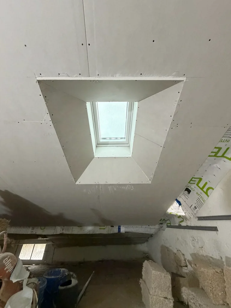 Plaques de plâtre vissées sous rampant et autour d'une fenêtre de toit, joints non finis