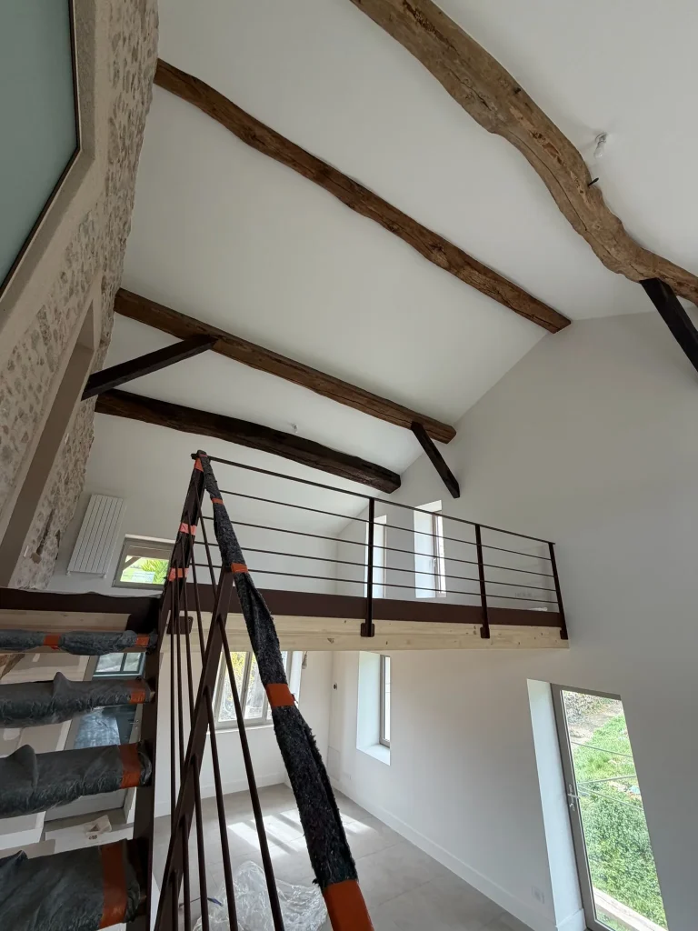 Pièce à mezzanine avec plafonds blancs entre poutres en bois et escabeau