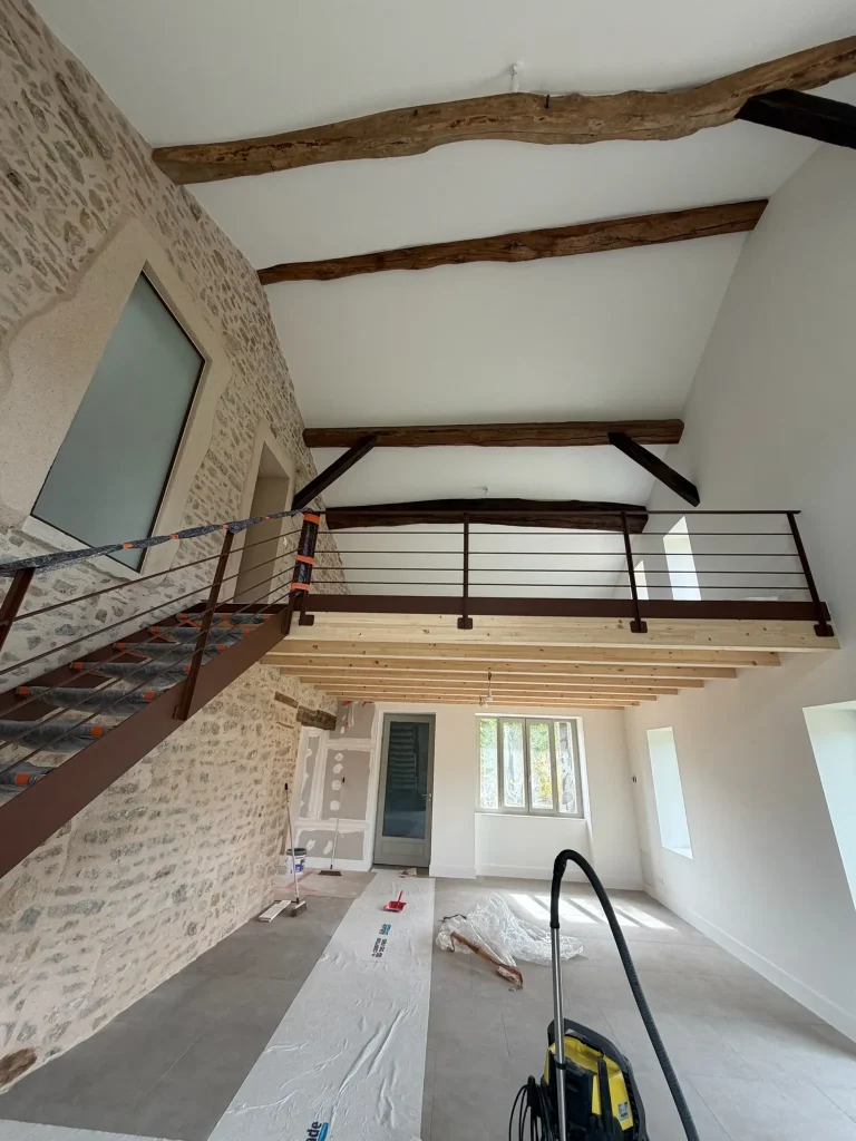 Pièce en rénovation avec plafond blanc, poutres apparentes et garde-corps de mezzanine