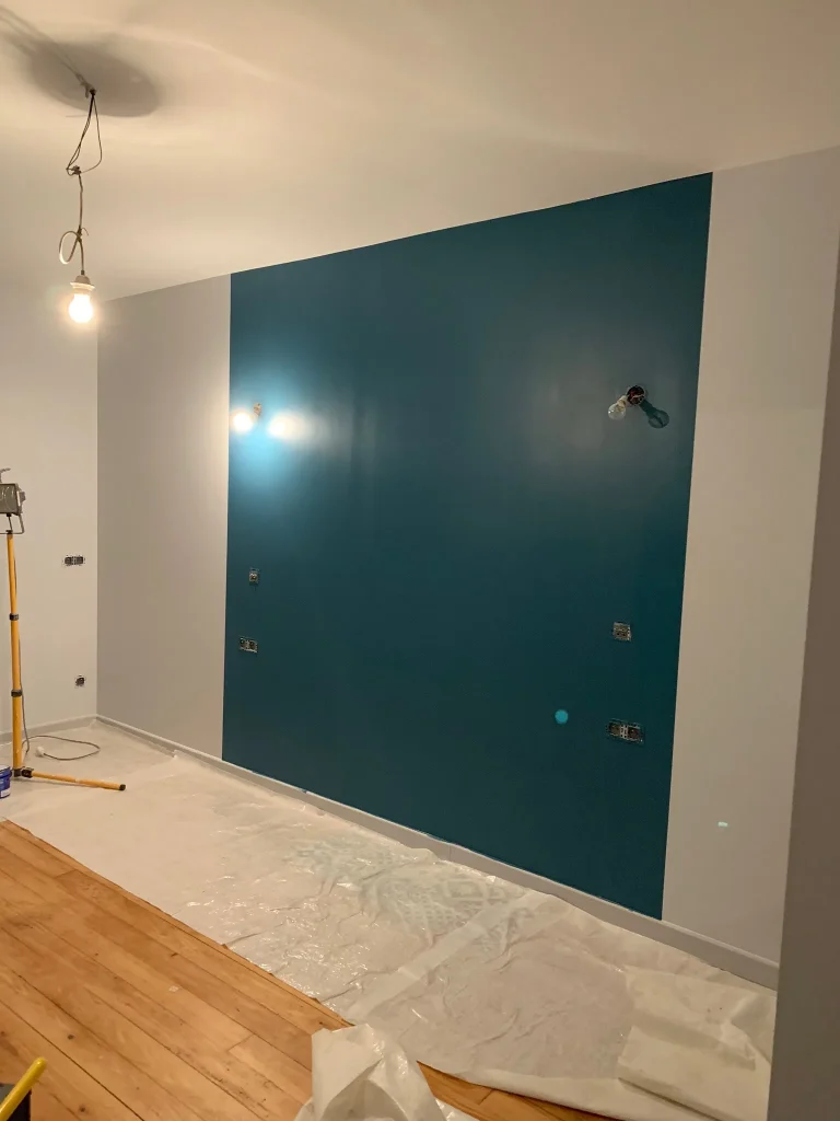 Mur intérieur bleu-vert, plafond blanc et sol protégé dans une pièce en rénovation