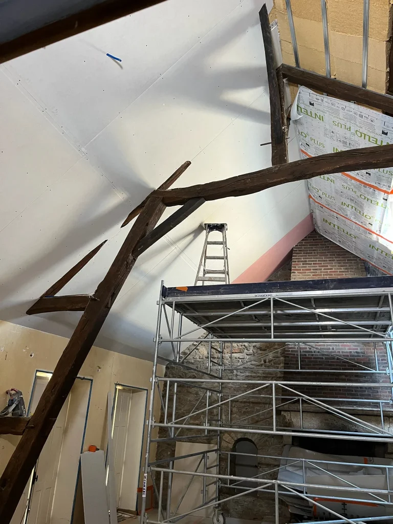 Chantier intérieur avec plaques de plâtre sous pente, isolant apparent, membrane et échafaudage