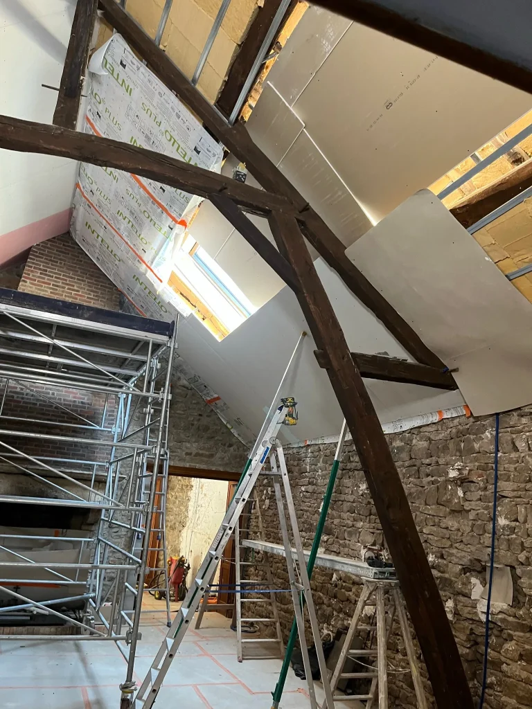 Combles en chantier avec plaques de plâtre, poutres en bois et échafaudage intérieur
