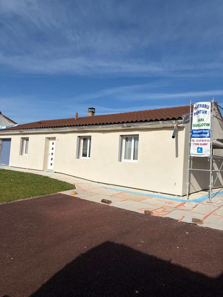Façade enduite claire d'un bâtiment de plain-pied, avec protections au sol et panneau Guillotin