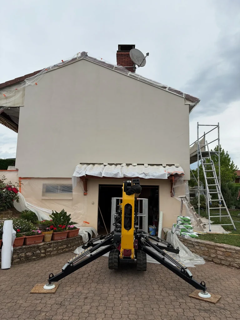 Pignon enduit clair avec matériel de chantier jaune devant la façade et échafaudage sur le côté