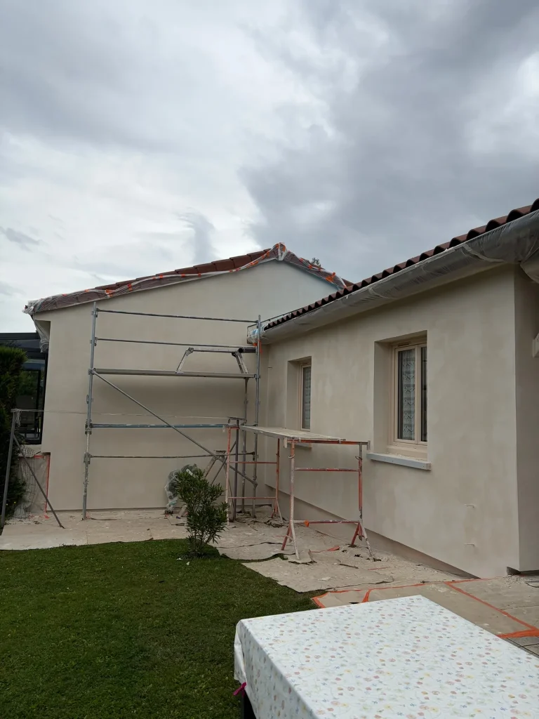Façade claire avec échafaudage et protections autour de la toiture, fenêtres et sol