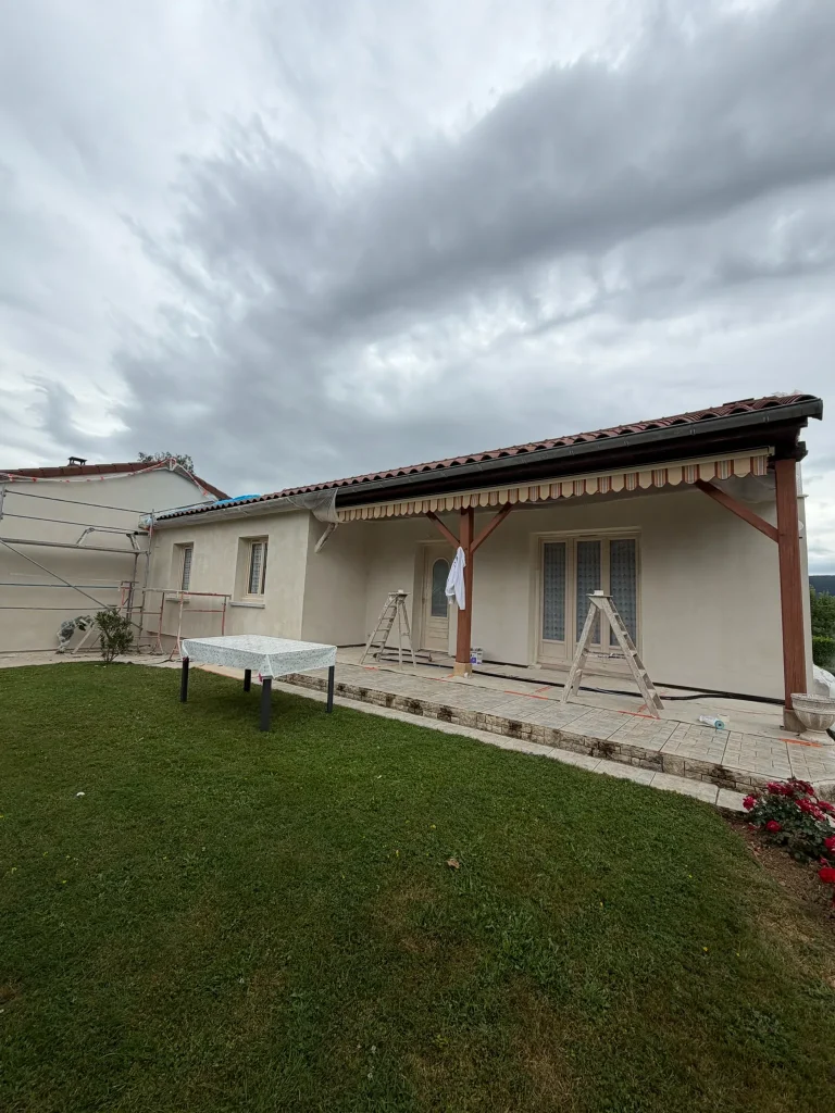 Façade claire d'une maison avec auvent en bois, terrasse, échelle et protections de chantier