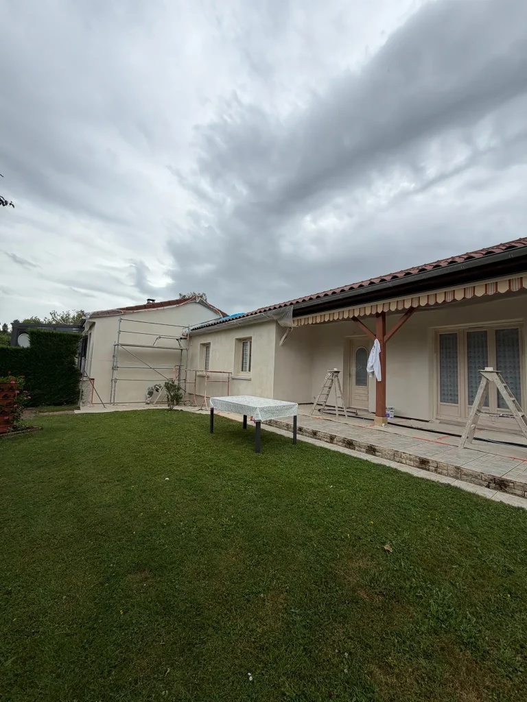 Façade enduite claire avec auvent, terrasse et échafaudage