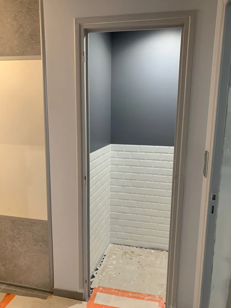 Petite pièce avec murs gris et soubassement mural à carreaux blancs, sol en cours de travaux