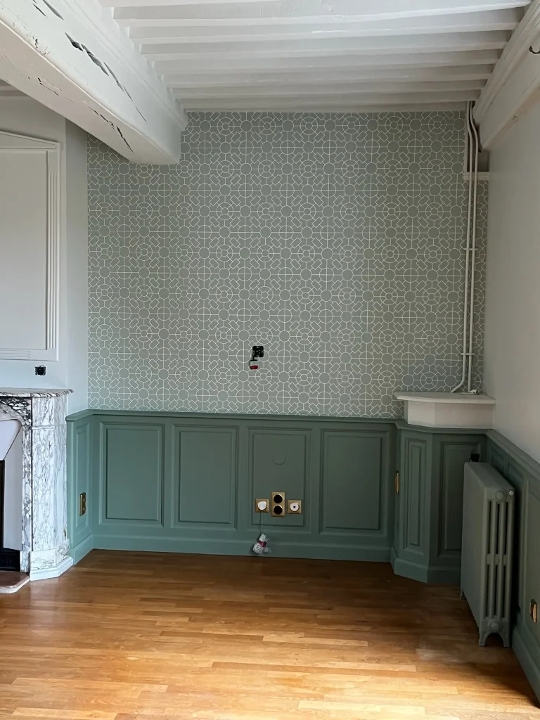 Papier peint à motifs au-dessus de boiseries vertes dans une pièce au plafond à poutres blanches