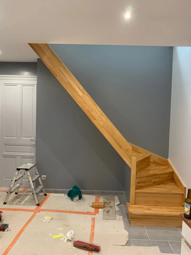 Escalier en bois devant un mur bleu-gris et blanc, avec protections de sol