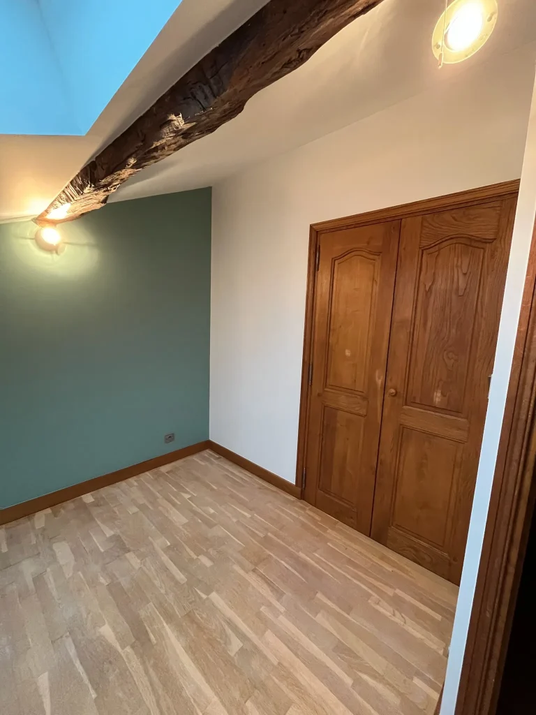 Pièce sous combles avec mur bleu-vert, plafond blanc, poutre et porte en bois