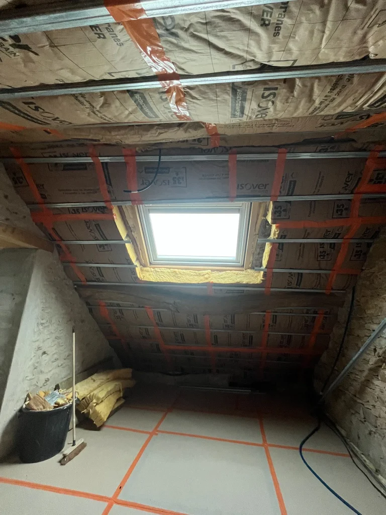 Isolant sous toiture avec ossature métallique et rubans de joint autour d'une fenêtre de toit