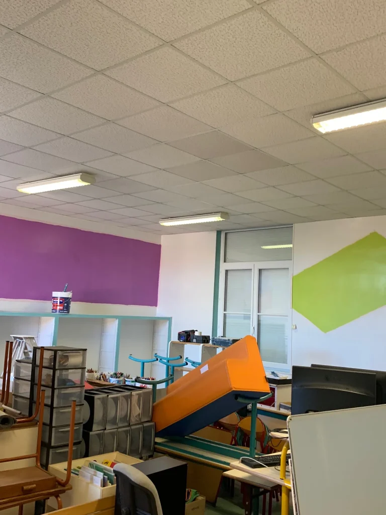 Intérieur en chantier aux murs mauves, blancs et verts, avec plafond en dalles et protections de mobilier