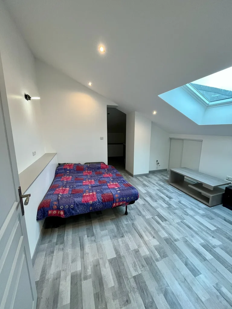 Chambre sous combles au sol effet bois gris, avec fenêtre de toit et literie colorée