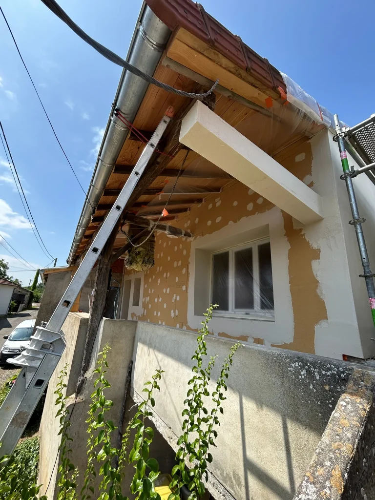 Façade avec panneaux d'isolant, enduit autour d'une fenêtre et échafaudage sous un auvent