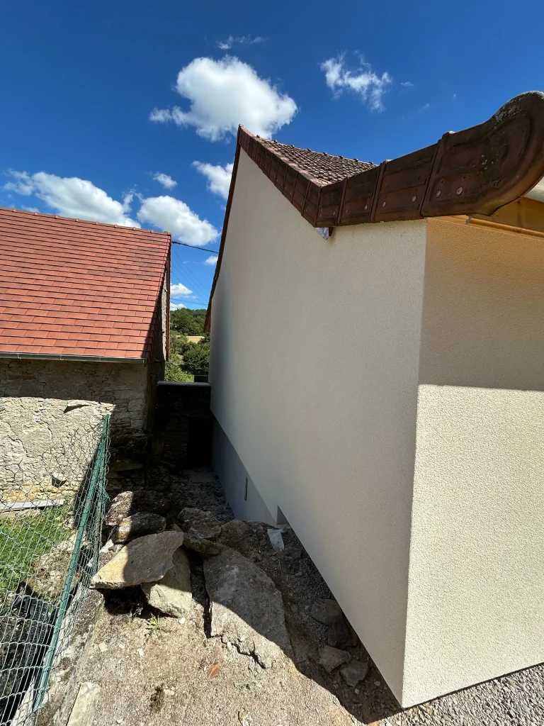 Pignon clair d'un bâtiment, avec toiture en tuiles et végétation au pied du mur