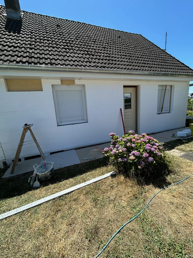 Façade claire d'une maison avec encadrements de fenêtres, volets fermés et échelle