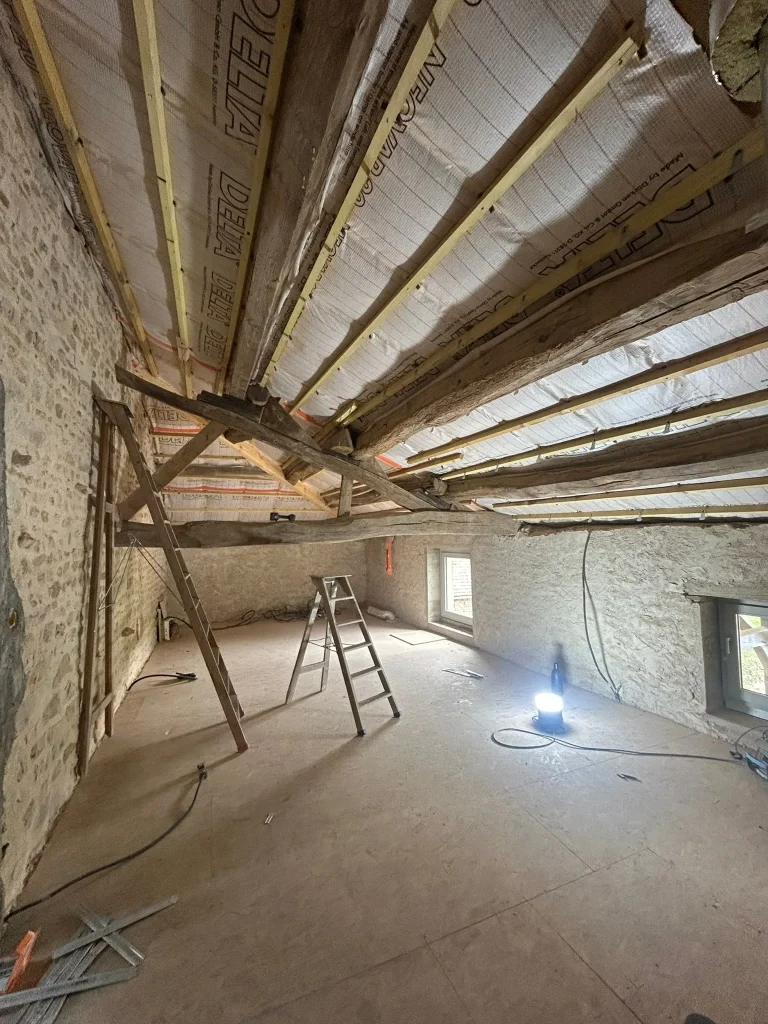 Membrane sous les rampants d'une toiture entre poutres en bois, avec escabeau et éclairage de chantier